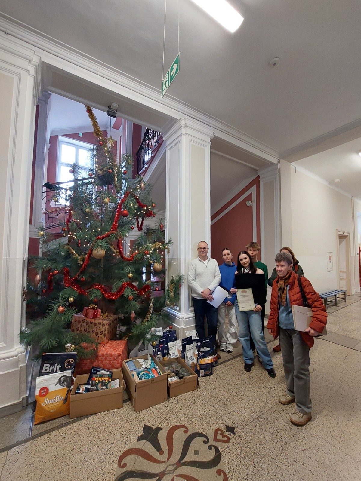 uczniowie i osoby z Fundacji stoją przed choinką, koło nich zebrane karmy