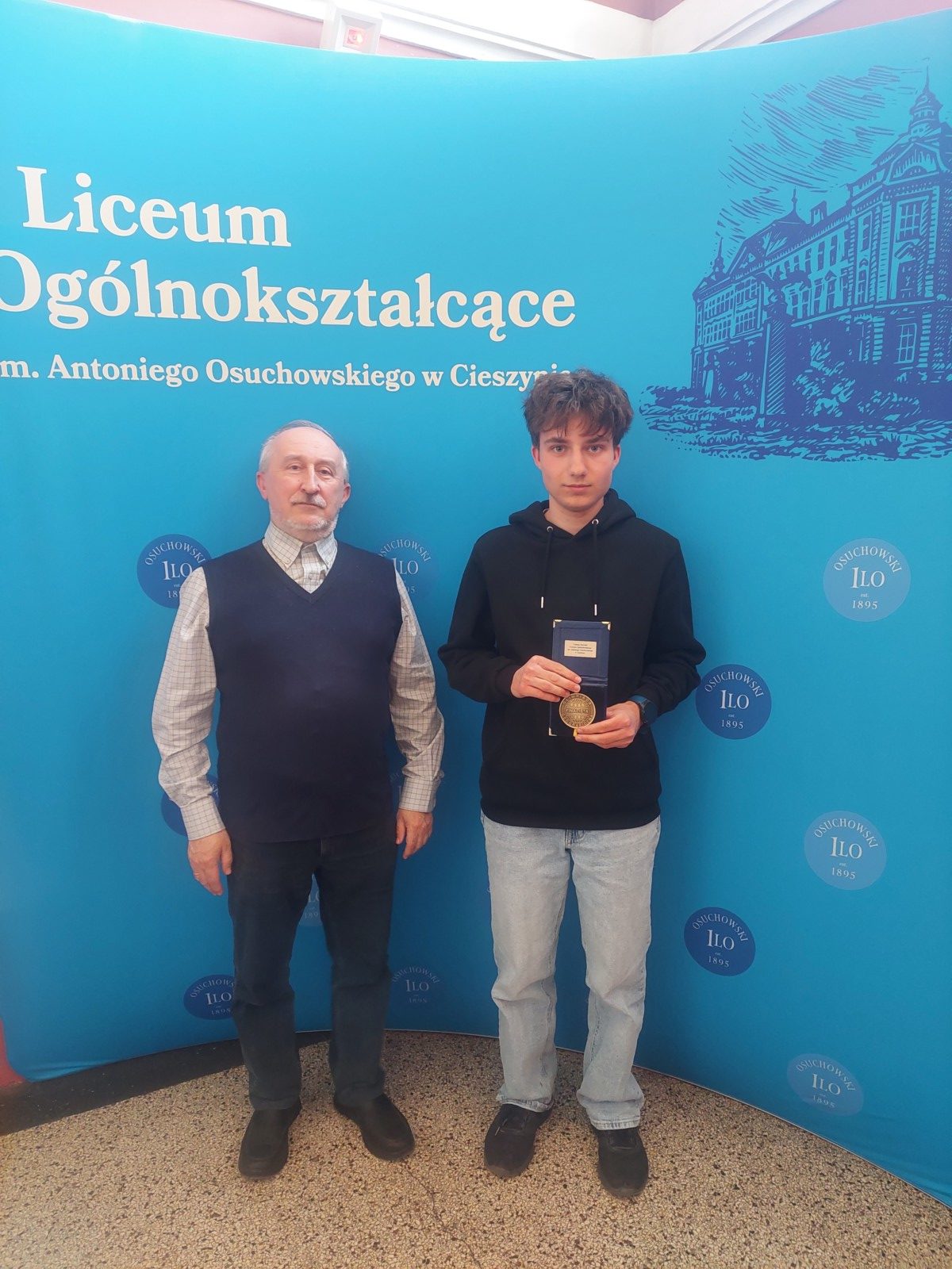 dwie osoby stoją przed ścianką szkoły